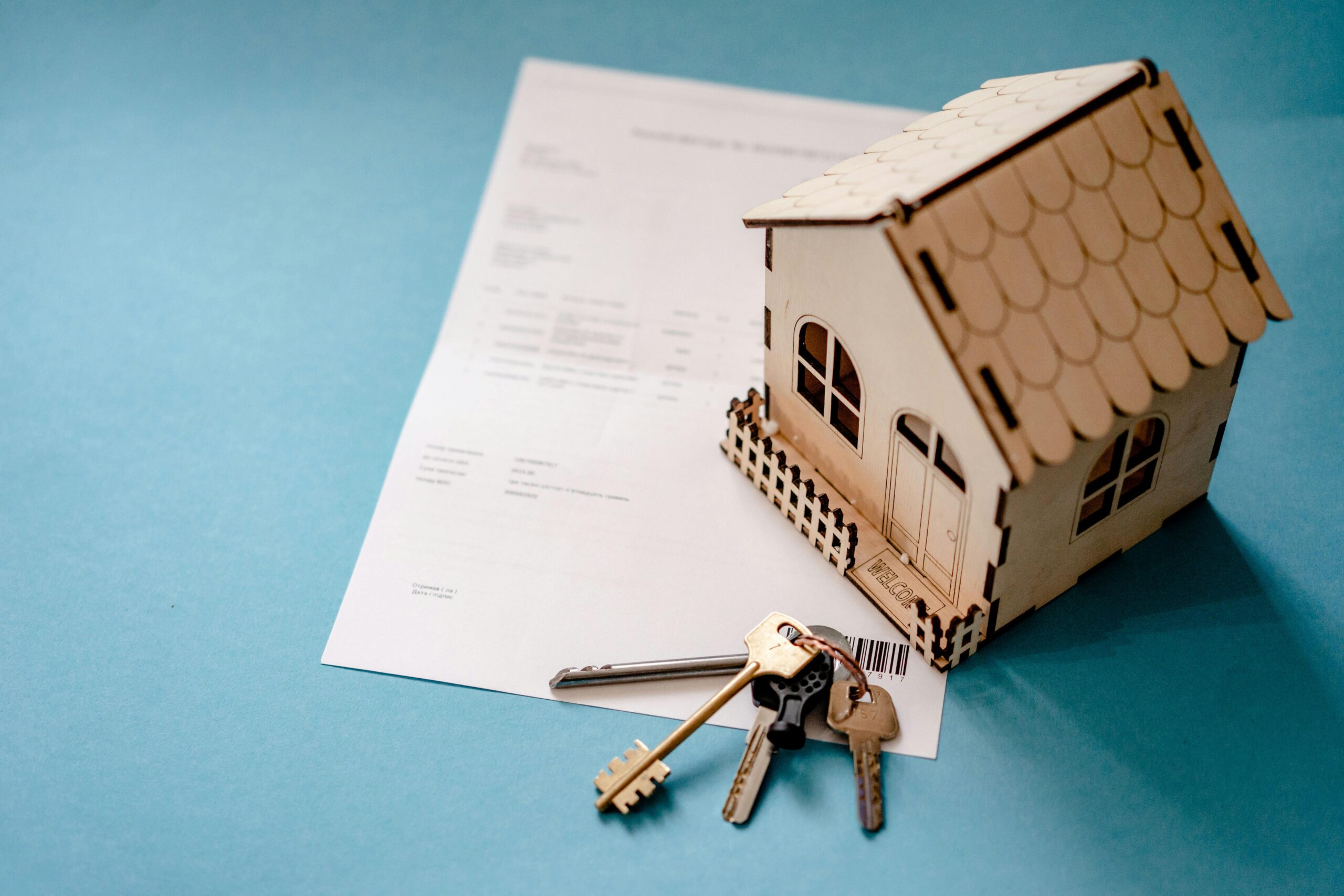 Miniature wooden house with keys and contract symbolizing real estate pro forma fail