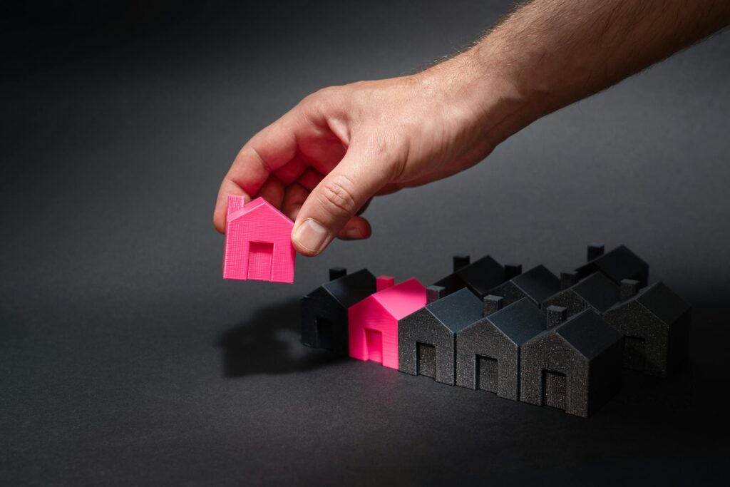 A hand selects a pink mini house among black models, symbolizing How Prediction Intelligence Is Revolutionizing Real Estate Development