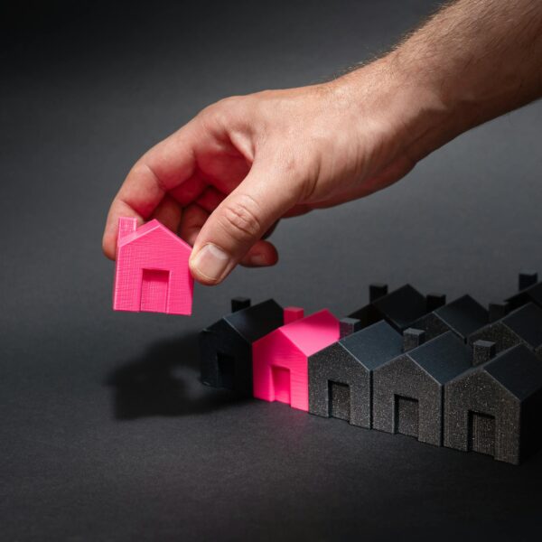 A hand selects a pink mini house among black models, symbolizing How Prediction Intelligence Is Revolutionizing Real Estate Development