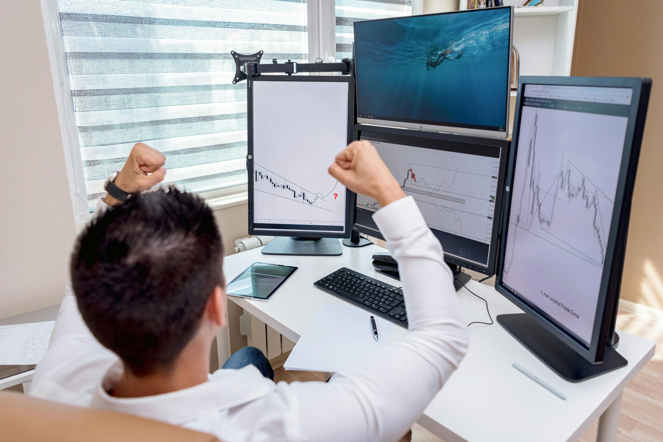A man celebrates in front of multiple computer monitors displaying stock market graphs, showing what Separate Winning Prediction Trades From Losses